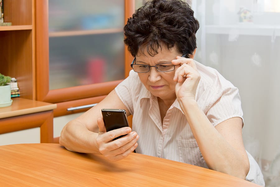 poor vision concept - elderly woman wearing reading glasses to look at her phone.