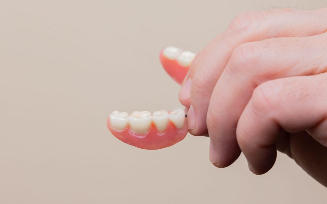 dentures in the hand of elderly man on tan backdrop