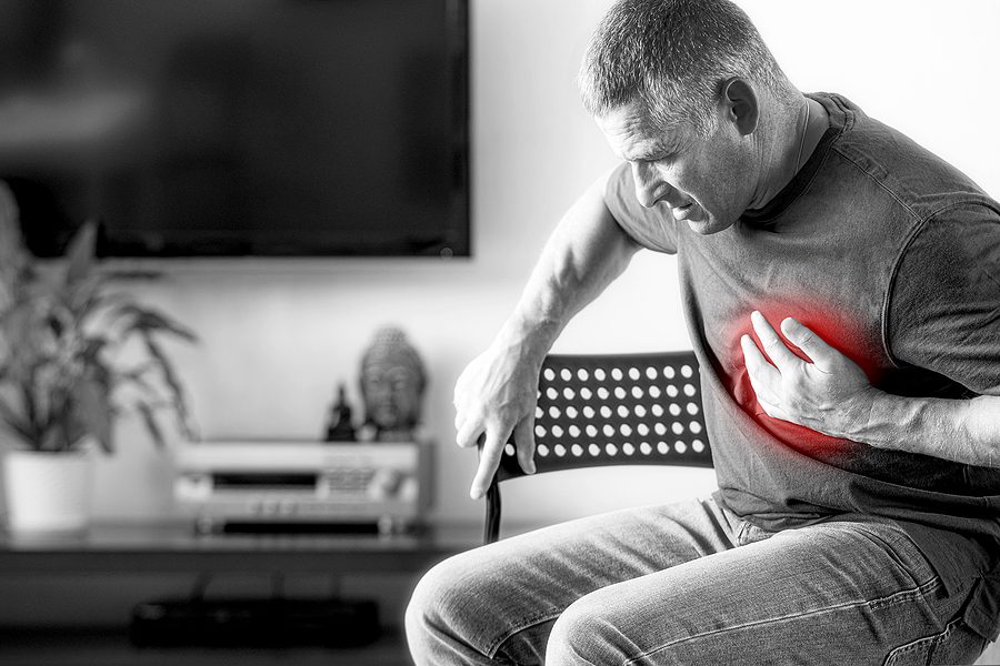 Heart disease concept - Black and white image of older man holding his heart, with the color red radiating over his chest.