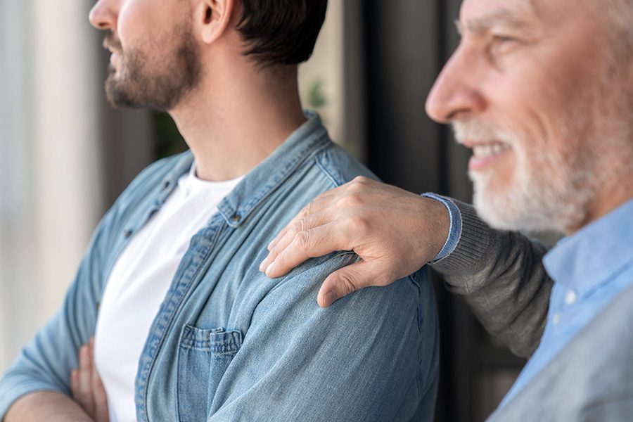 close up of elderly man holding his son's shoulder - career setbacks for family caregiver concept