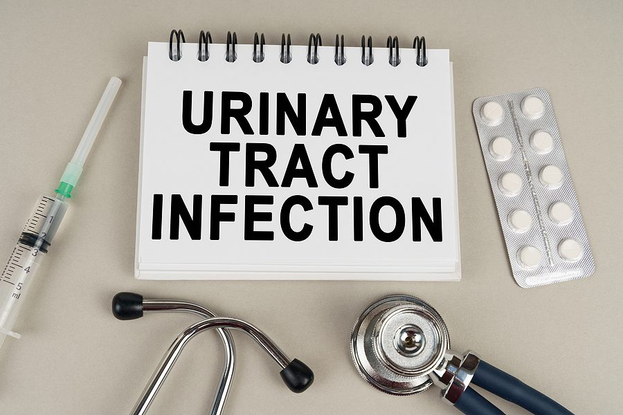 On a gray surface, a syringe, thermometer, stethoscope, blister and notepad with inscription - Urinary tract infection - UTIs concept