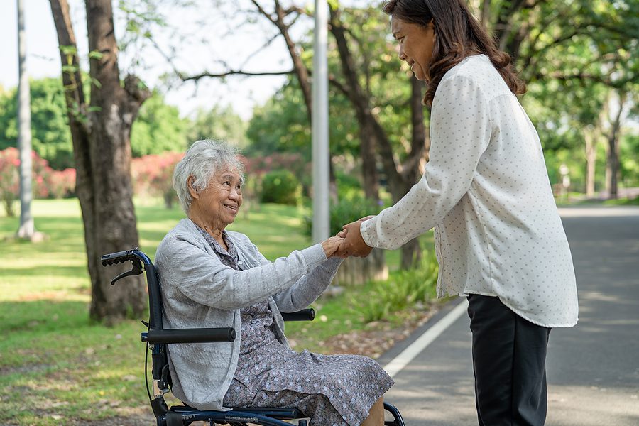 caregiver with positive smile helping elderly woman in wheelchair in the park