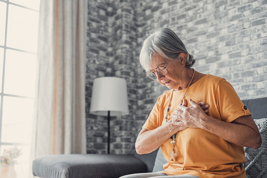 elderly woman clutching heart in pain - heart failure concept