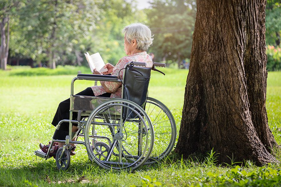 older woman in a wheelchair reading outside in the summer