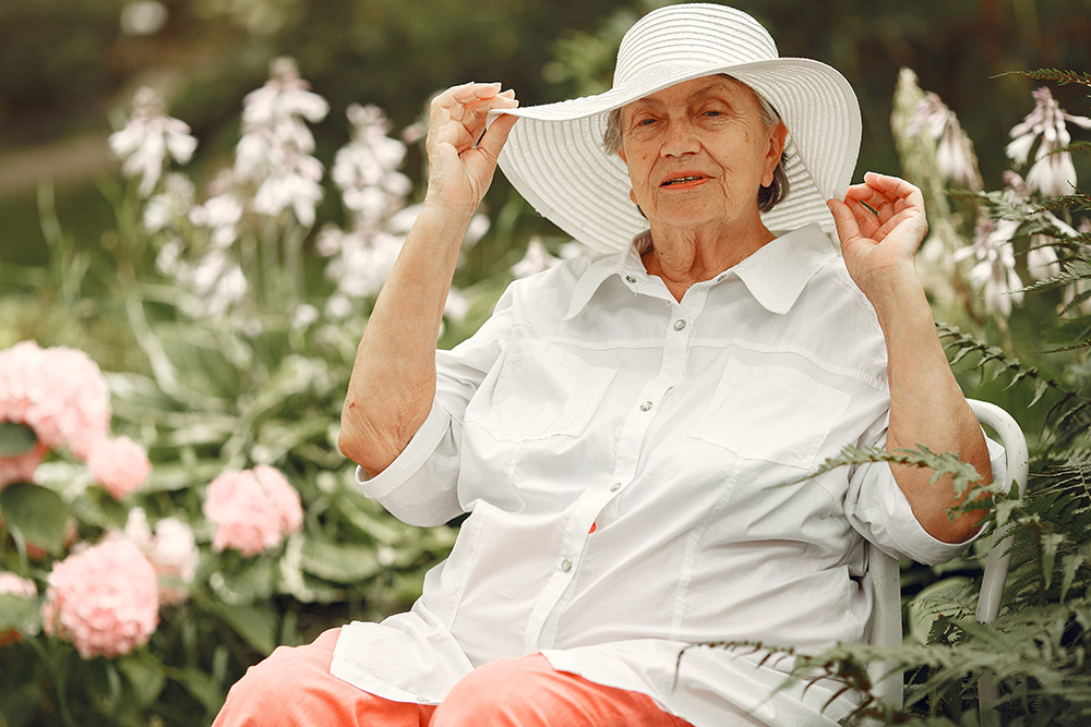 older woman in a field of flowers in a white sunhat and blouse - sun safety for older people