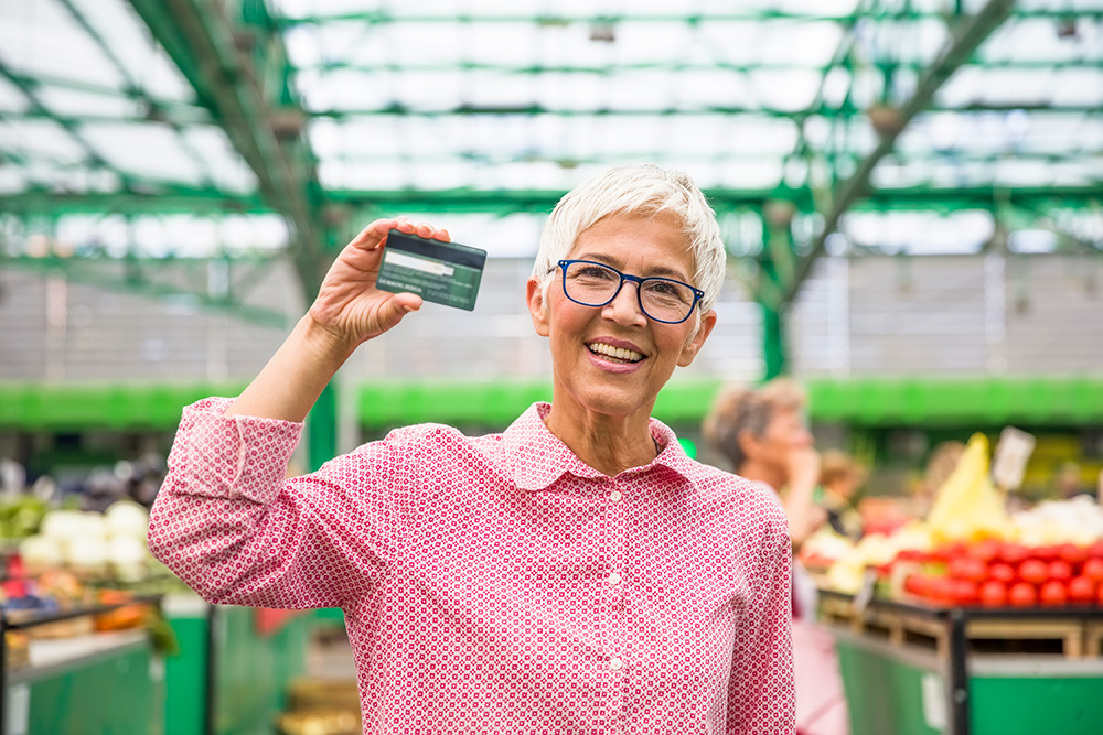 older woman in grocery store holds up credit card - credit score for retirees concept