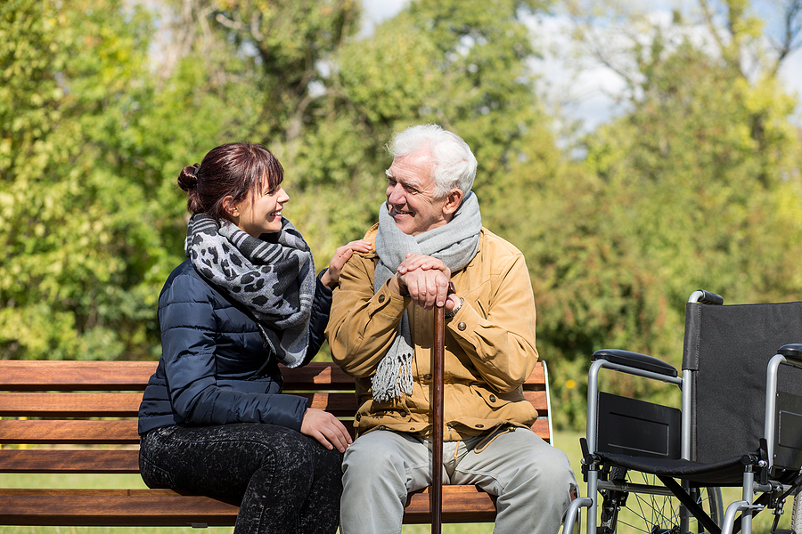 older adult man and family caregiver in scarves on a park bench