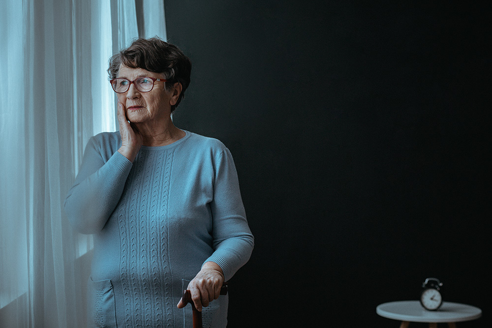 elder woman with cane looking out a window while sad -social isolation in older adults concept