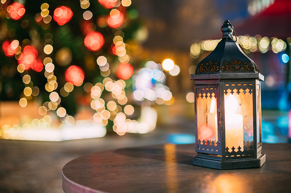 candle lantern burning on a table in front of bokeh winter holiday lights - dementia care and the holidays concept