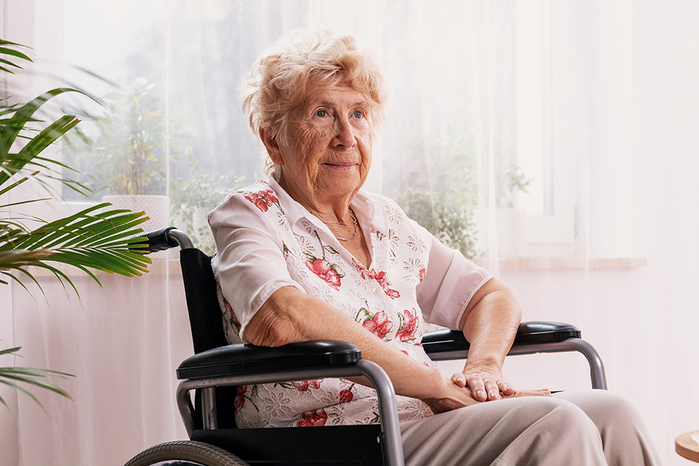 older woman in a wheelchair by a window - dementia stages concept