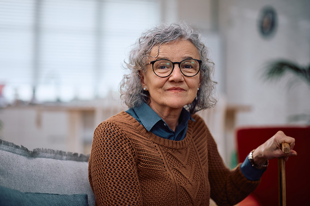 elder woman sitting at home holding her cane - stroke prevention tips concept