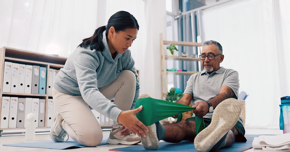 physical therapist assists older man with leg exercise using a green resistance band - physical therapy concept