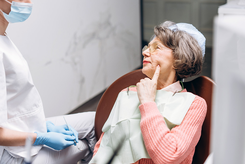 older woman pointing to her cheek in the dentist's chair - dental care for elders