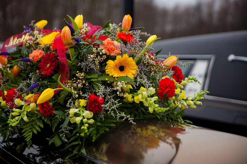 funeral flower arrangement on top of a casket near a hearse - grief and loss of an elderly loved one concept